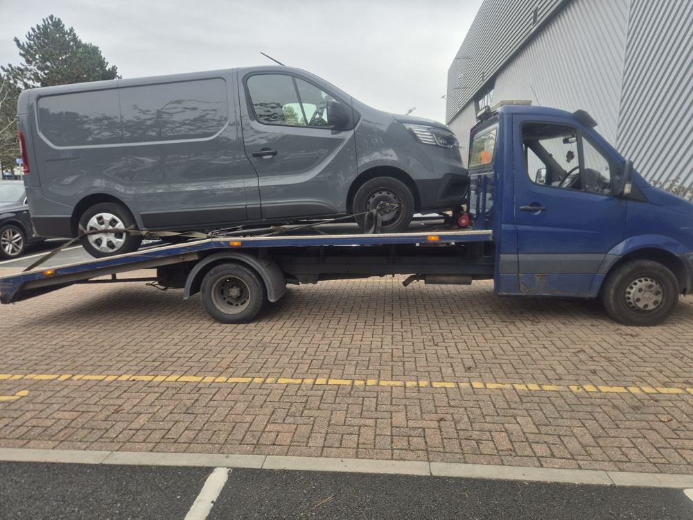Grey panel van strapped down on a recovery truck